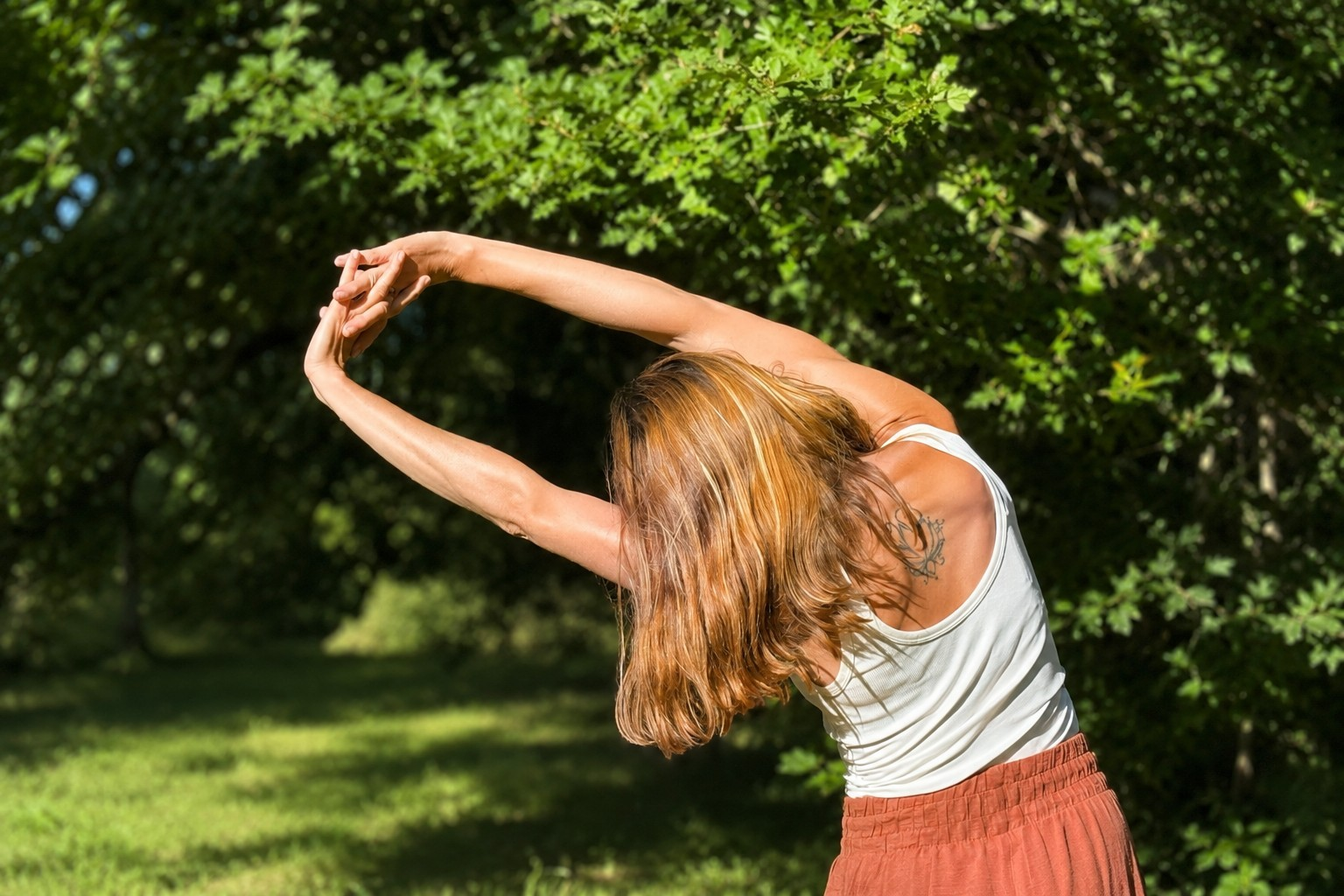 Mujer realizando un estiramiento de costado al aire libre entre la vegetación